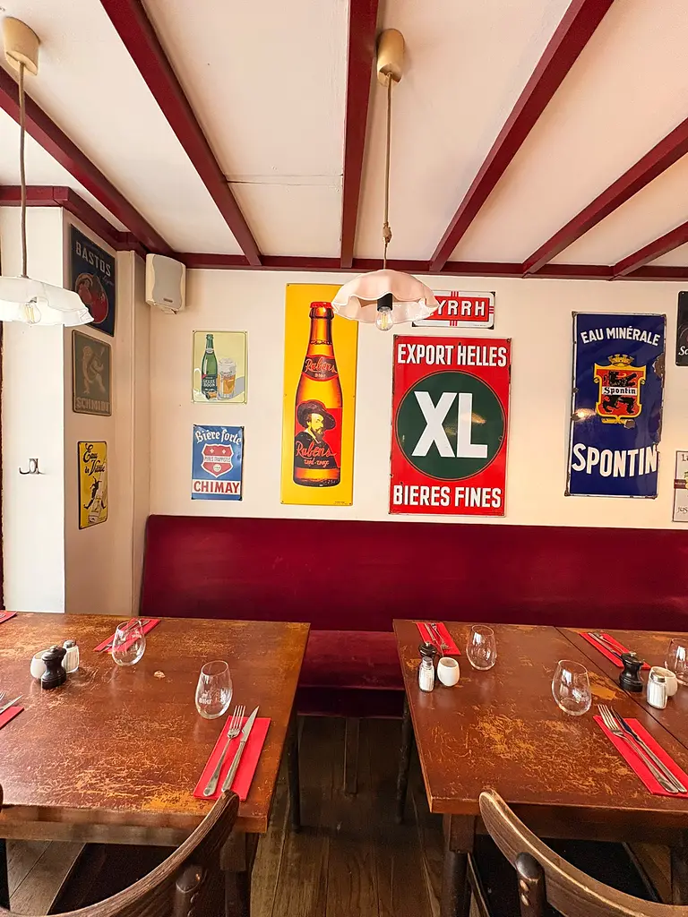 Mur de plaques émaillées de brasseries belges au-dessus d’une banquette bordeaux, dans la salle des Brassins.